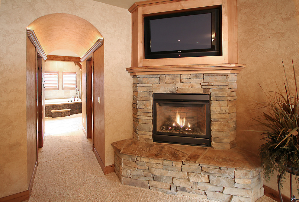 Modelo de sala de estar cerrada rústica de tamaño medio con paredes beige, moqueta, chimenea de esquina, marco de chimenea de piedra y pared multimedia