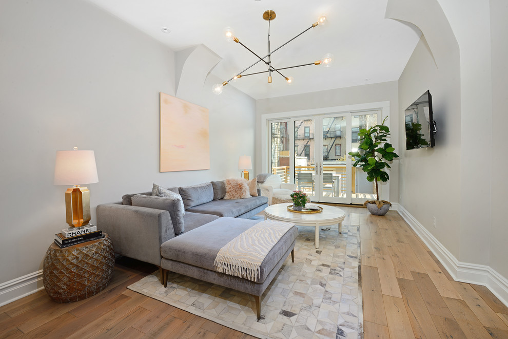 Ejemplo de sala de estar abierta contemporánea con paredes grises, suelo de madera clara, televisor colgado en la pared y suelo beige