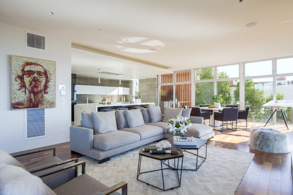 Diseño de sala de estar abierta contemporánea extra grande con paredes blancas, suelo de madera en tonos medios, marco de chimenea de madera y televisor retractable