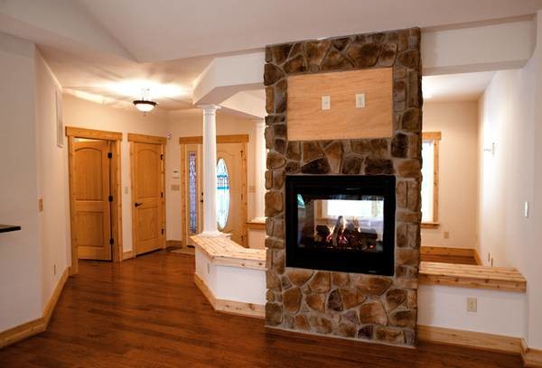 Imagen de sala de estar abierta rústica con paredes beige, suelo de madera en tonos medios, chimenea de doble cara, marco de chimenea de piedra y televisor colgado en la pared