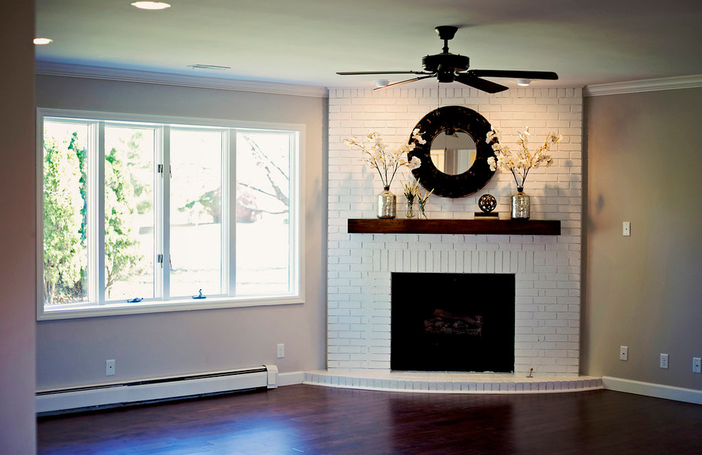 Ejemplo de sala de estar abierta clásica grande con paredes grises, suelo de madera en tonos medios, chimenea de esquina y marco de chimenea de ladrillo