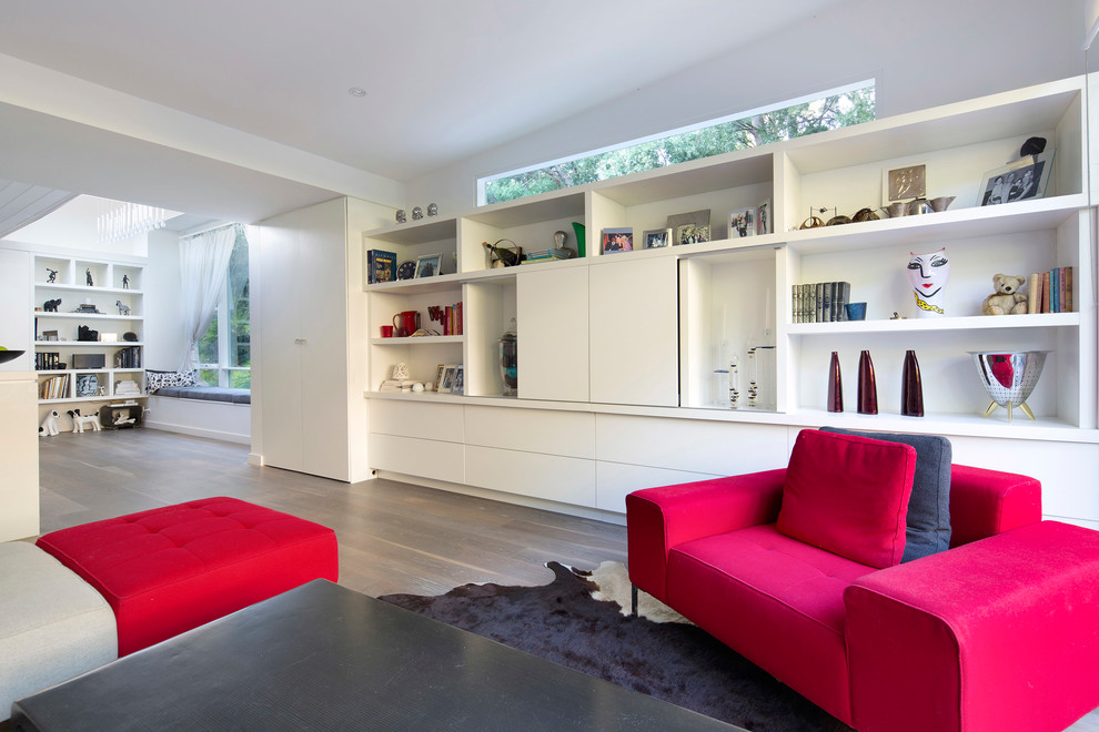 Modelo de sala de estar abierta actual de tamaño medio con paredes blancas, suelo de madera clara, televisor retractable y suelo blanco