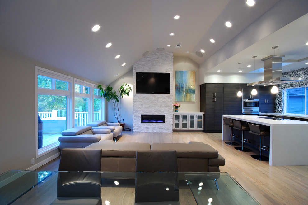 Diseño de sala de estar abierta contemporánea grande con paredes grises, suelo de madera clara, todas las chimeneas, marco de chimenea de piedra y televisor colgado en la pared