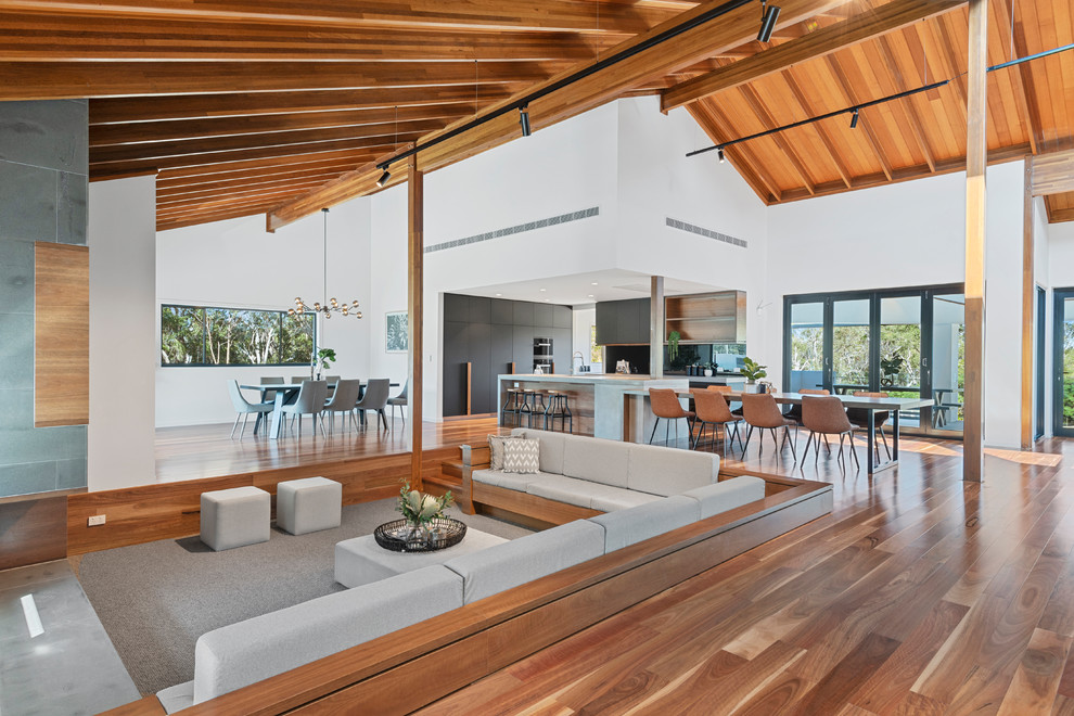 This is an example of a large contemporary open plan games room in Brisbane with medium hardwood flooring, white walls and a wooden fireplace surround.
