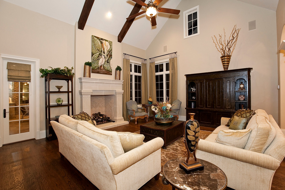 Diseño de sala de estar abierta clásica con paredes beige, suelo de madera oscura, todas las chimeneas y marco de chimenea de piedra