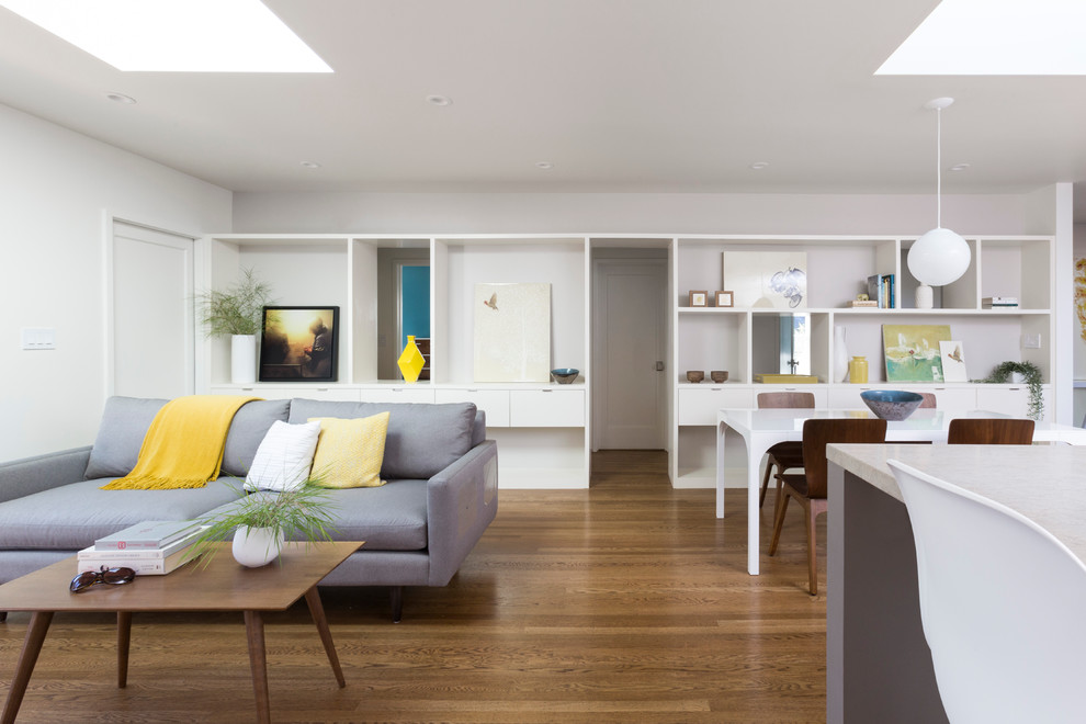 Diseño de sala de estar abierta moderna de tamaño medio sin chimenea con paredes grises, suelo de madera oscura y televisor colgado en la pared