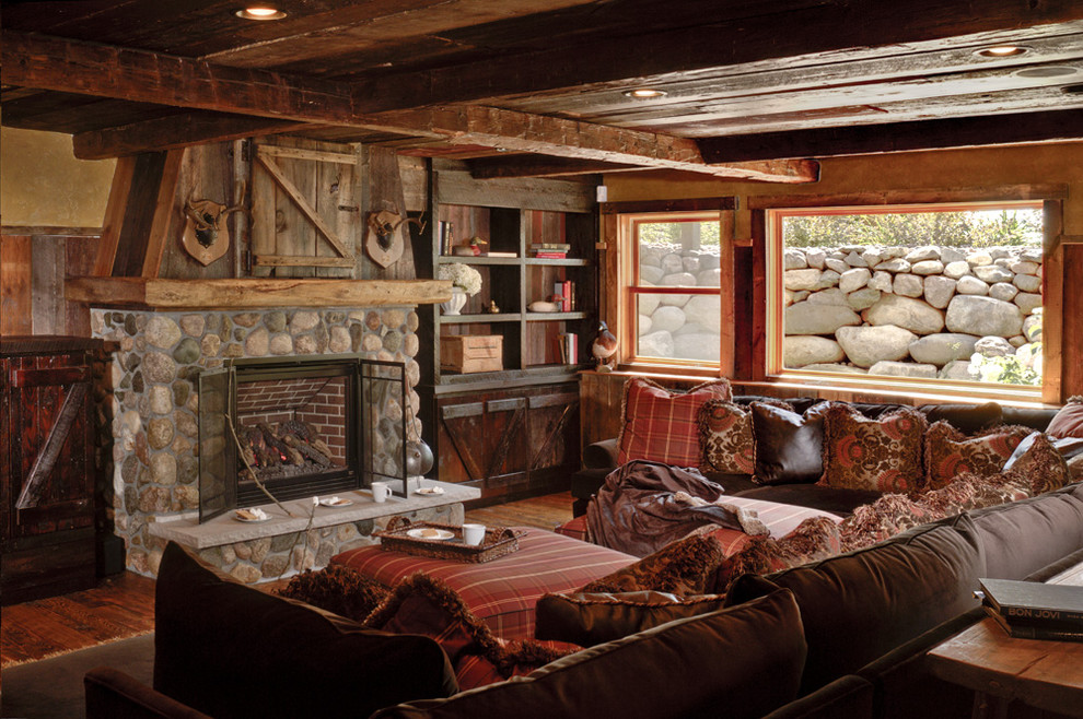 Abgetrenntes Rustikales Wohnzimmer mit brauner Wandfarbe, dunklem Holzboden, Kamin und Kaminumrandung aus Stein in Minneapolis