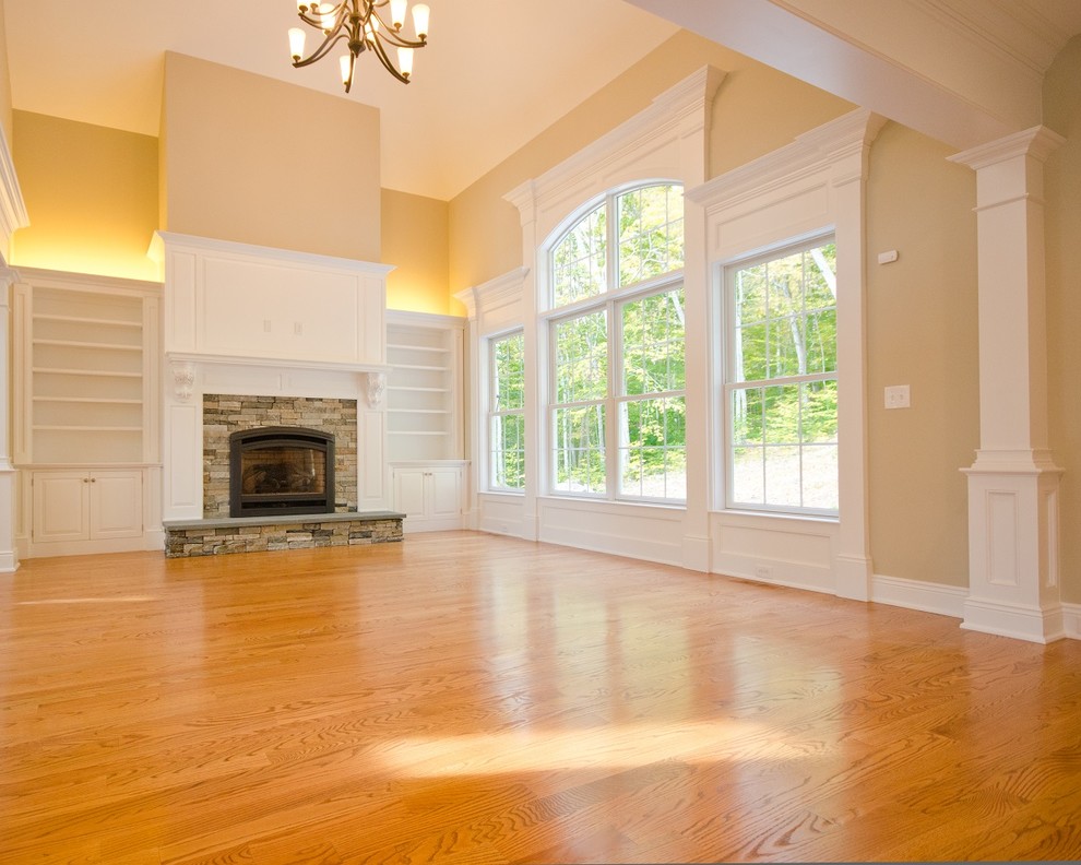 Mittelgroßes Klassisches Wohnzimmer mit beiger Wandfarbe, braunem Holzboden, Kamin, Kaminumrandung aus Stein und braunem Boden in Bridgeport