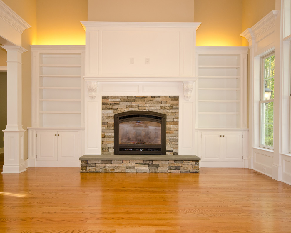 Aménagement d'une salle de séjour classique de taille moyenne avec un mur beige, un sol en bois brun, une cheminée standard, un manteau de cheminée en pierre et un sol marron.