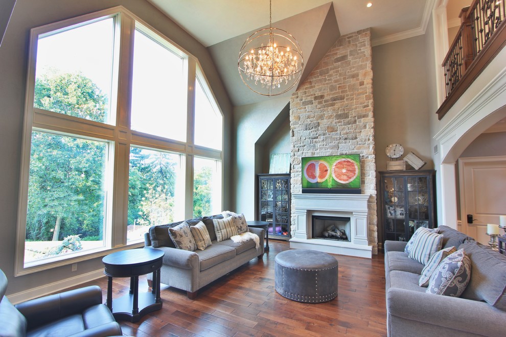 Diseño de sala de estar abierta clásica renovada grande con paredes grises, suelo de madera en tonos medios, todas las chimeneas, marco de chimenea de yeso y televisor colgado en la pared