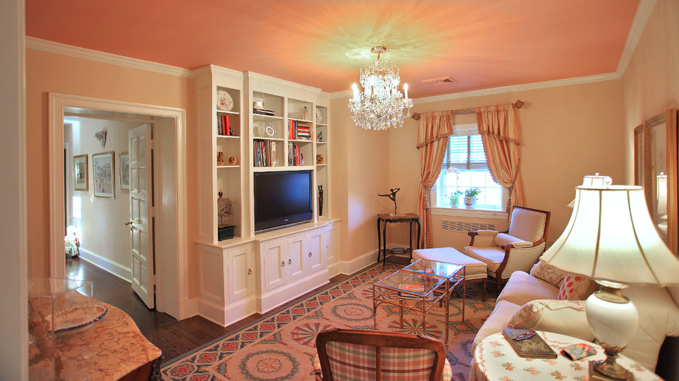 Cette photo montre une salle de séjour chic de taille moyenne et fermée avec une bibliothèque ou un coin lecture, un mur rose, parquet foncé et un téléviseur encastré.