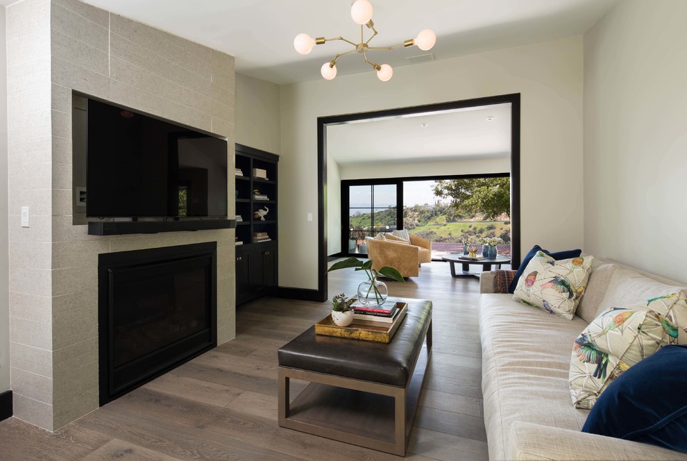 Пример оригинального дизайна: открытая гостиная комната среднего размера в современном стиле с серыми стенами, паркетным полом среднего тона, стандартным камином, фасадом камина из плитки, телевизором на стене и серым полом