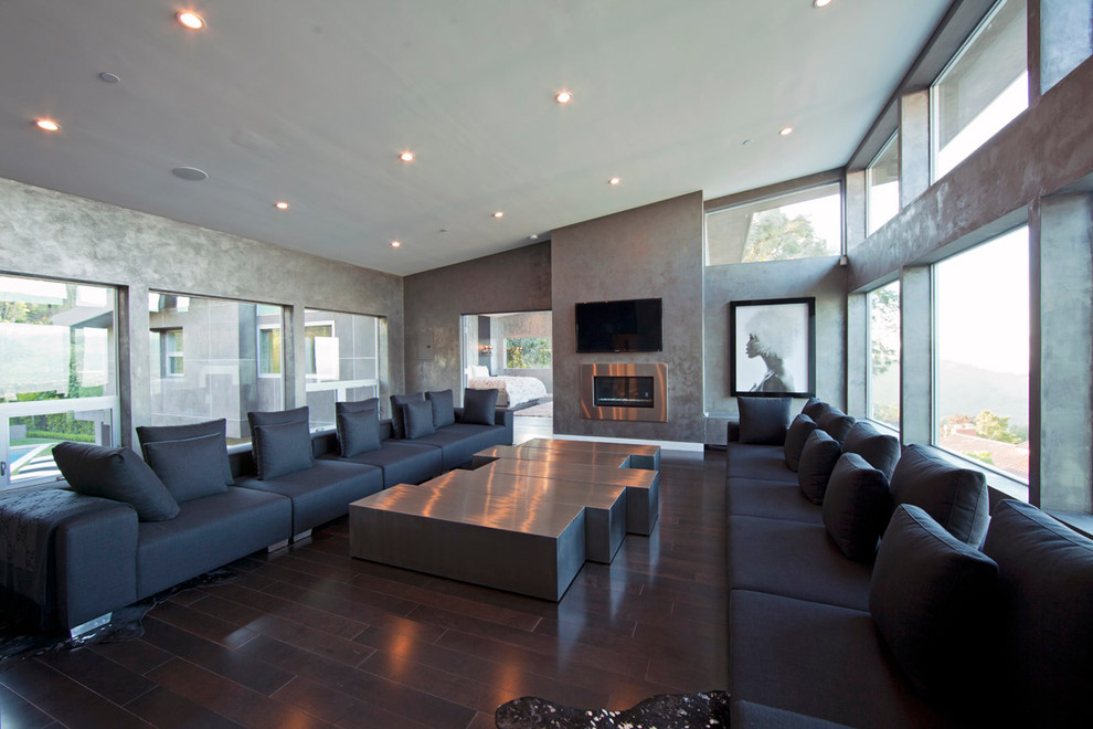 Diseño de sala de estar abierta actual con paredes grises, suelo de madera oscura, marco de chimenea de metal y televisor colgado en la pared