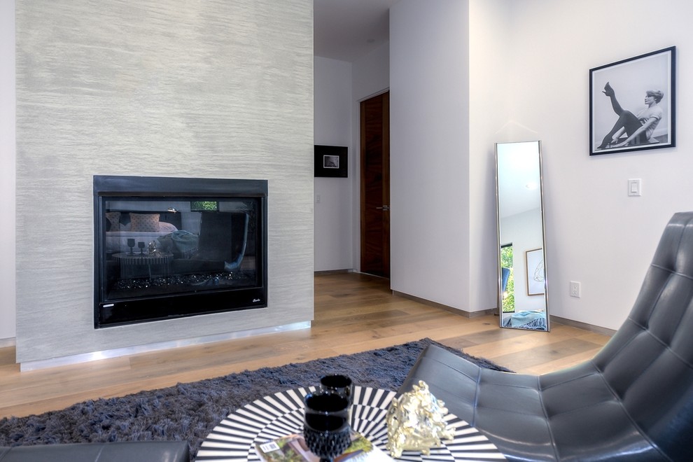 Imagen de sala de estar abierta moderna grande sin televisor con paredes blancas, suelo de madera clara, todas las chimeneas y marco de chimenea de hormigón