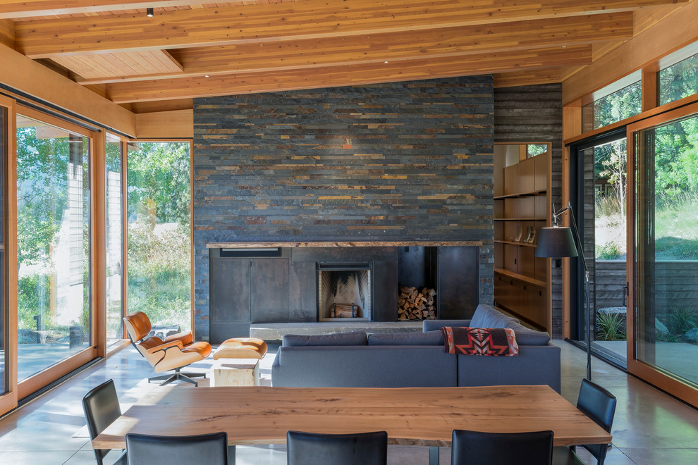 Cette photo montre une salle à manger montagne de taille moyenne avec sol en béton ciré, une cheminée standard, un manteau de cheminée en métal et un sol gris.