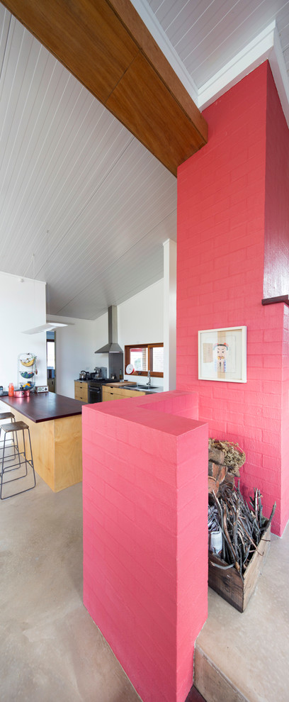 Cette photo montre une petite salle de séjour tendance ouverte avec sol en béton ciré, une cheminée standard, un manteau de cheminée en brique et un mur rose.