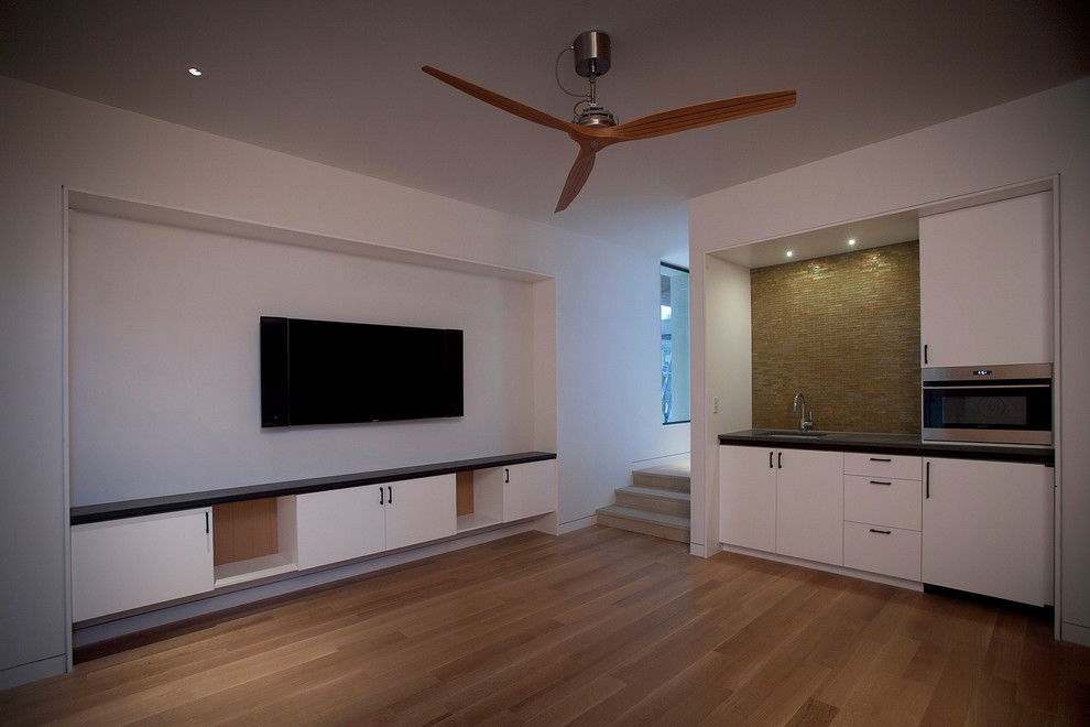 Réalisation d'une grande salle de séjour minimaliste ouverte avec un mur blanc, un sol en bois brun, un téléviseur encastré et un sol multicolore.