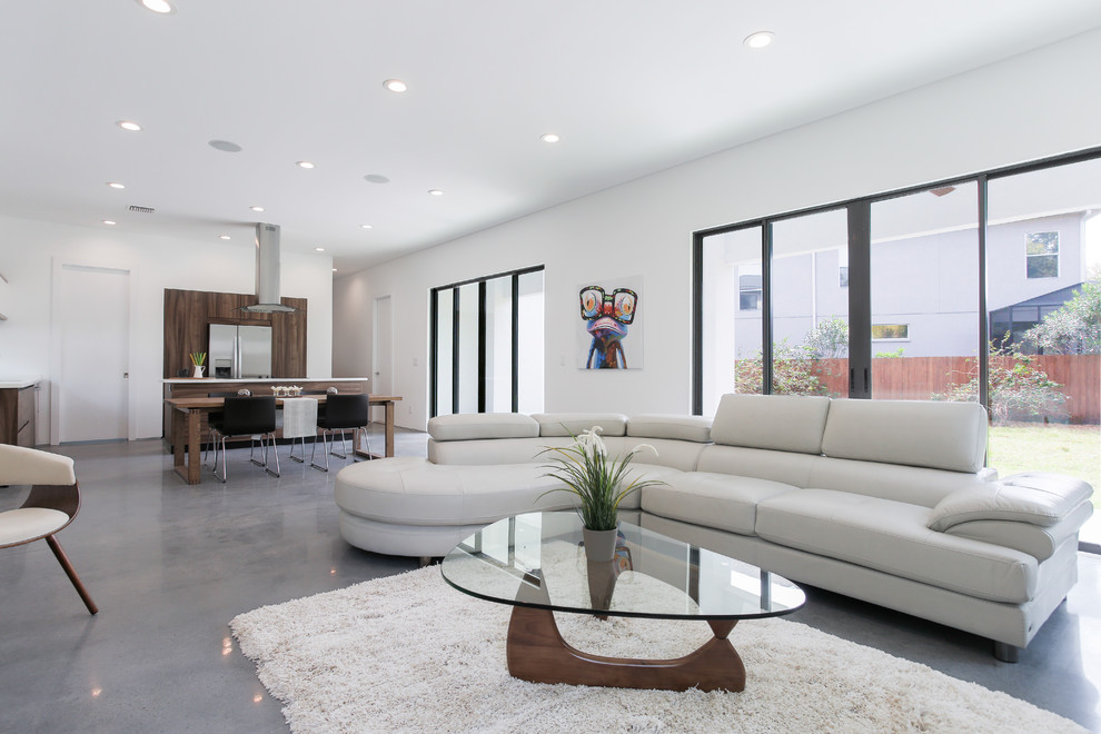 Стильный дизайн: огромная открытая гостиная комната в стиле модернизм с белыми стенами, бетонным полом и телевизором на стене - последний тренд