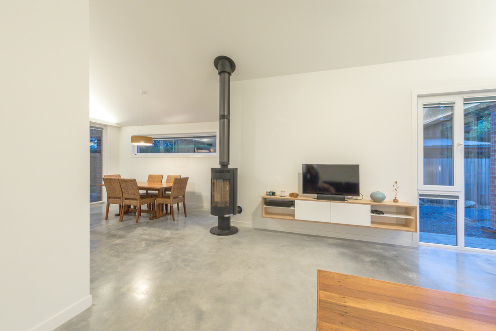 Foto de sala de estar abierta actual pequeña con paredes blancas, suelo de cemento, estufa de leña, marco de chimenea de hormigón y suelo gris