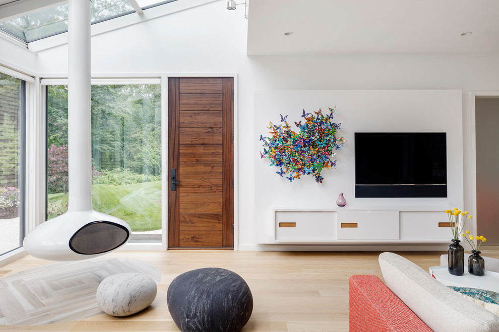 Immagine di un soggiorno minimal di medie dimensioni e aperto con pareti bianche, parquet chiaro, camino sospeso, TV a parete e pavimento beige