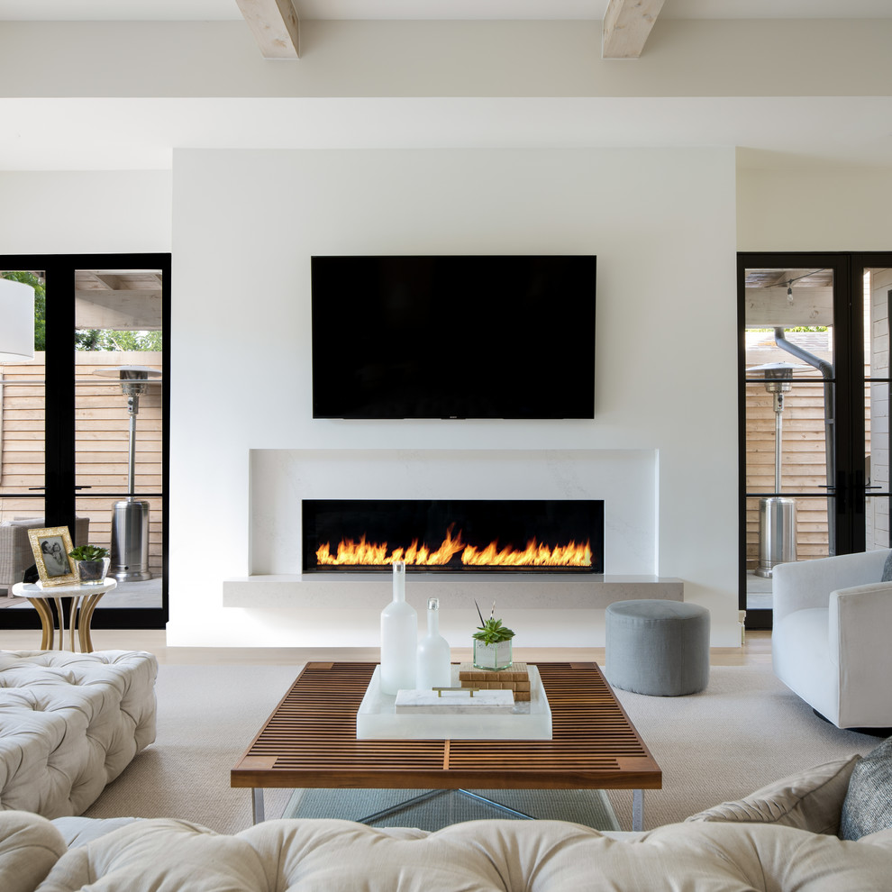 Imagen de sala de estar abierta contemporánea grande con paredes blancas, suelo de madera clara, chimenea lineal, televisor colgado en la pared, suelo beige y marco de chimenea de yeso