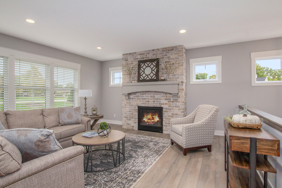 Cette photo montre une salle de séjour nature ouverte et de taille moyenne avec un mur gris, un sol en vinyl, une cheminée standard, un manteau de cheminée en brique, un sol marron et aucun téléviseur.