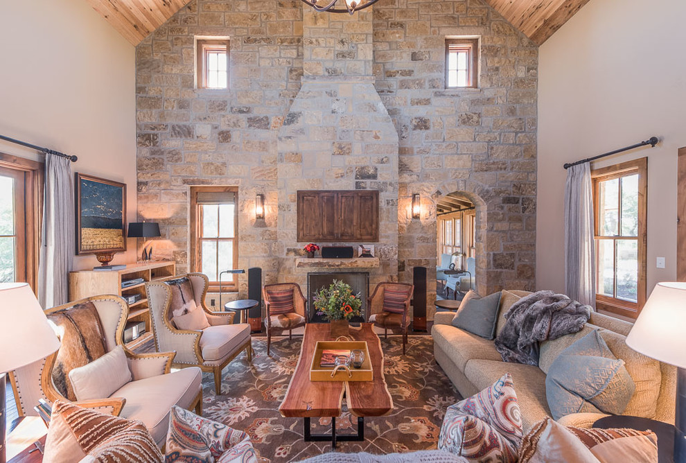 Rustikales Wohnzimmer mit beiger Wandfarbe, Kamin, Kaminumrandung aus Stein und verstecktem TV in Austin