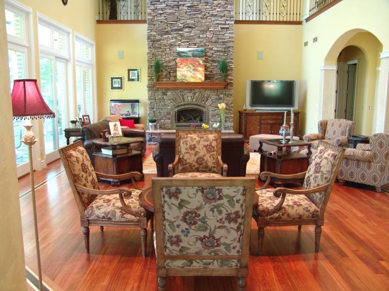 Cette image montre une grande salle de séjour traditionnelle ouverte avec un mur jaune, un sol en bois brun, une cheminée standard, un manteau de cheminée en pierre et un téléviseur indépendant.