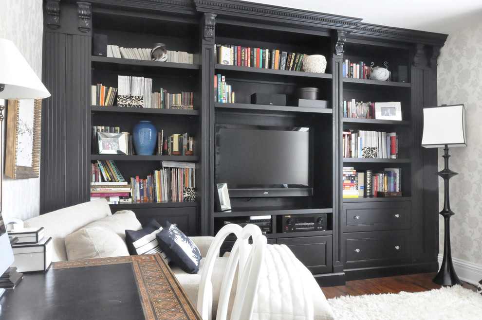 Imagen de sala de estar con biblioteca cerrada clásica pequeña sin chimenea con paredes blancas, suelo de madera oscura y pared multimedia