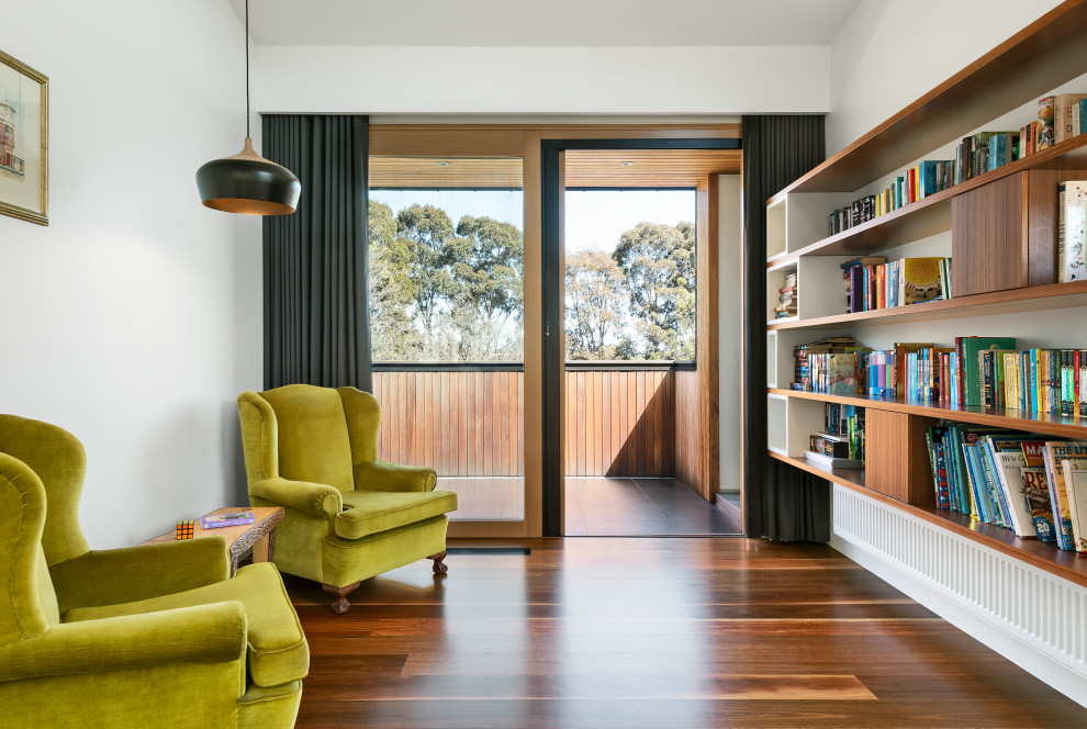 Aménagement d'une très grande salle de séjour contemporaine avec une bibliothèque ou un coin lecture, un mur blanc, un sol en bois brun et un sol marron.