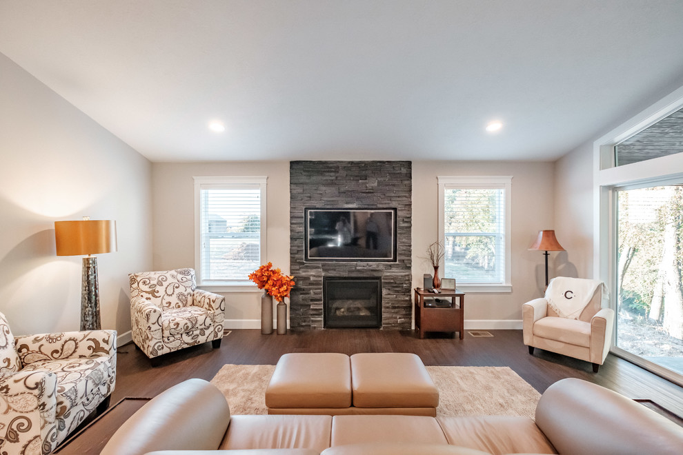 Example of a trendy open concept brown floor family room design in Portland with beige walls, a standard fireplace, a stone fireplace and a wall-mounted tv