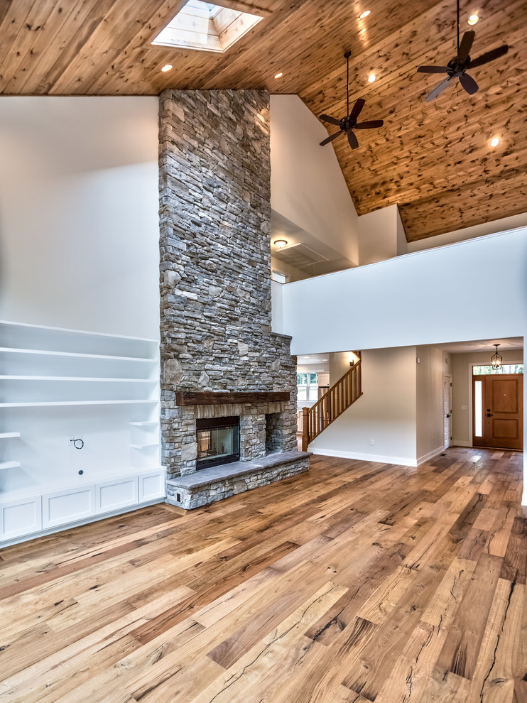 Large classic mezzanine games room in Other with medium hardwood flooring, a two-sided fireplace, a stone fireplace surround, a built-in media unit, grey walls and brown floors.