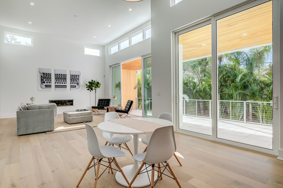 Modelo de sala de estar abierta moderna grande con paredes blancas, suelo de madera clara, chimenea lineal, marco de chimenea de metal y suelo beige