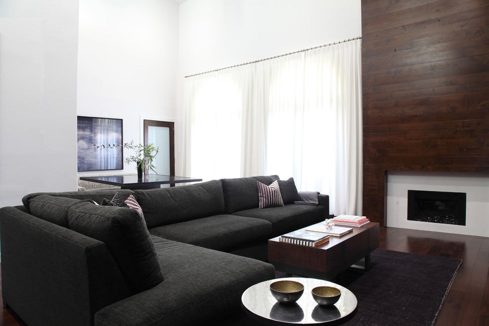 Imagen de sala de estar abierta actual grande con paredes grises, suelo de madera oscura, televisor colgado en la pared, todas las chimeneas y marco de chimenea de madera