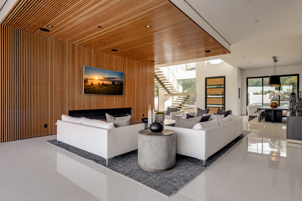 ロサンゼルスにある高級な巨大なコンテンポラリースタイルのおしゃれなオープンリビング (磁器タイルの床、木材の暖炉まわり、壁掛け型テレビ、白い床、茶色い壁、標準型暖炉) の写真