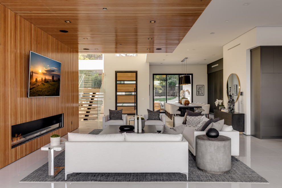 ロサンゼルスにある高級な巨大なコンテンポラリースタイルのおしゃれなオープンリビング (茶色い壁、磁器タイルの床、標準型暖炉、木材の暖炉まわり、壁掛け型テレビ、白い床) の写真