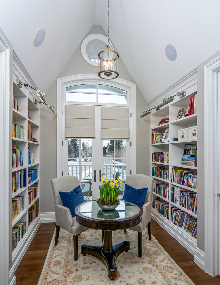 Cette image montre une salle de séjour traditionnelle avec une bibliothèque ou un coin lecture, parquet foncé et un mur gris.