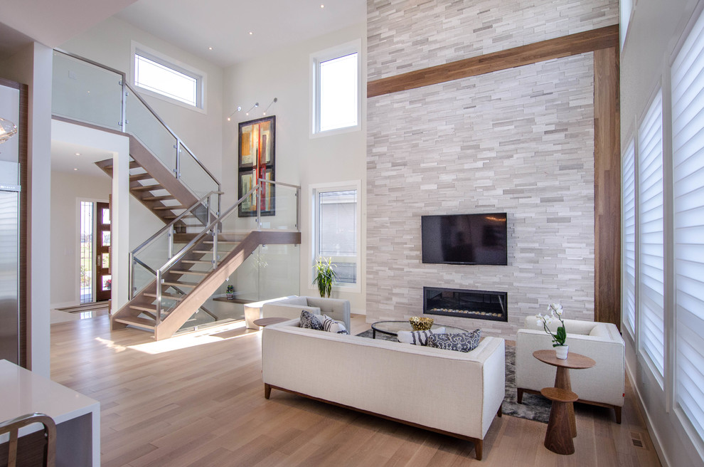 Modelo de sala de estar abierta contemporánea con paredes grises, televisor colgado en la pared, suelo de madera clara y chimenea lineal