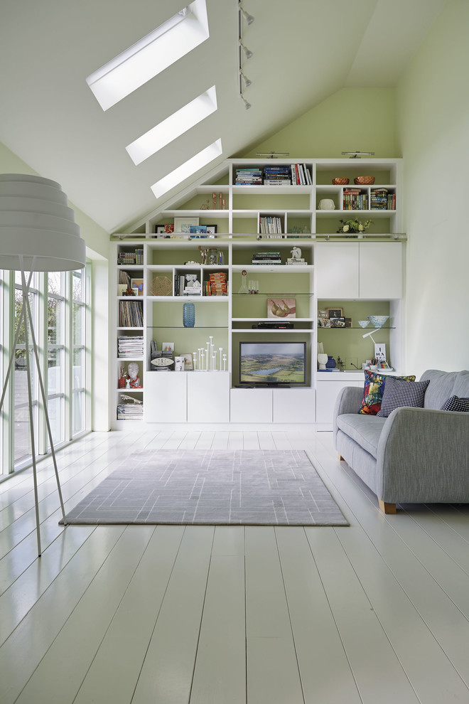 Cette photo montre une salle de séjour tendance ouverte avec une bibliothèque ou un coin lecture, un mur vert, parquet clair, un téléviseur encastré et un sol blanc.