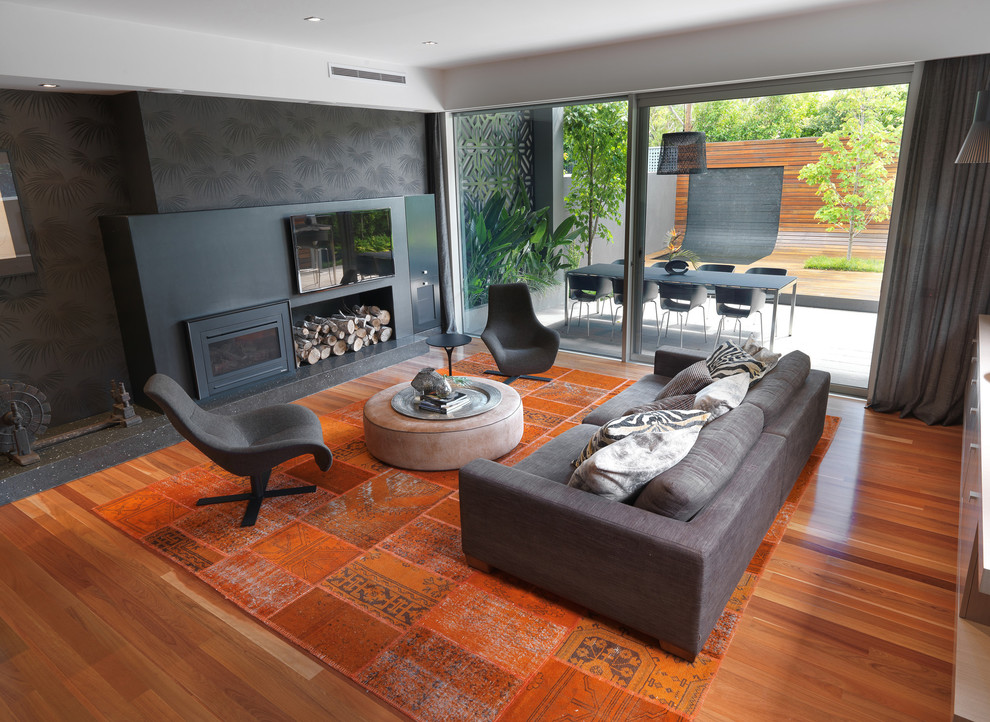 Diseño de sala de estar abierta contemporánea grande con paredes negras, suelo de madera en tonos medios, televisor colgado en la pared, estufa de leña, marco de chimenea de metal y suelo naranja
