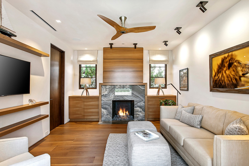 Example of a mid-sized trendy enclosed medium tone wood floor and brown floor family room design in Los Angeles with white walls, a standard fireplace, a wall-mounted tv and a stone fireplace