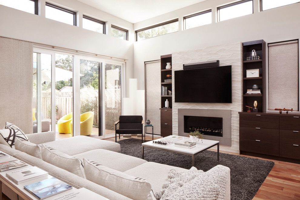Imagen de sala de estar abierta contemporánea con paredes grises, suelo de madera en tonos medios, televisor colgado en la pared y chimenea lineal