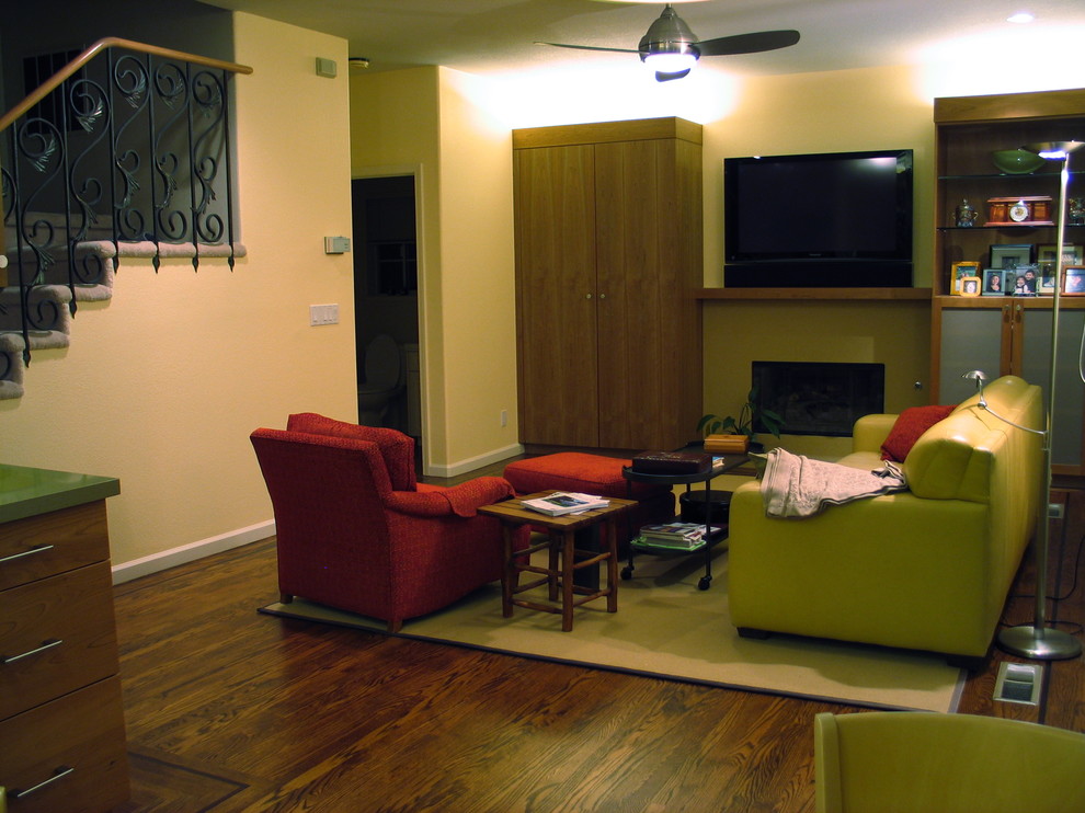 Пример оригинального дизайна: большая открытая гостиная комната в современном стиле с желтыми стенами, темным паркетным полом, мультимедийным центром, коричневым полом, стандартным камином и фасадом камина из штукатурки