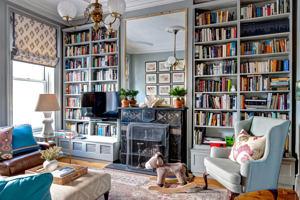 Imagen de sala de estar con biblioteca tradicional de tamaño medio con paredes verdes, suelo de madera en tonos medios y marco de chimenea de piedra