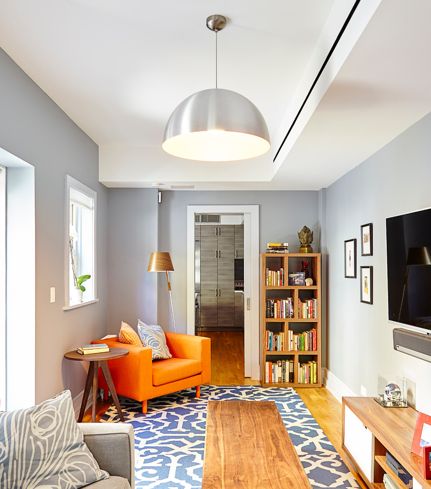 Esempio di un soggiorno minimal di medie dimensioni e chiuso con pareti grigie, libreria, parquet chiaro e TV a parete