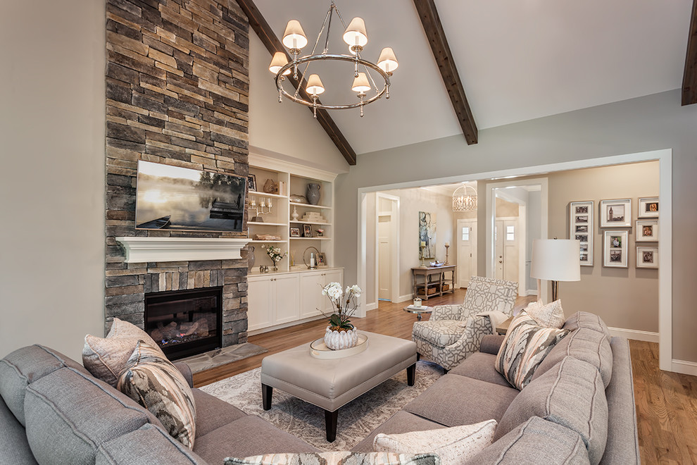 Foto de sala de estar abierta tradicional renovada grande con paredes grises, suelo de madera clara, todas las chimeneas, marco de chimenea de piedra y televisor colgado en la pared