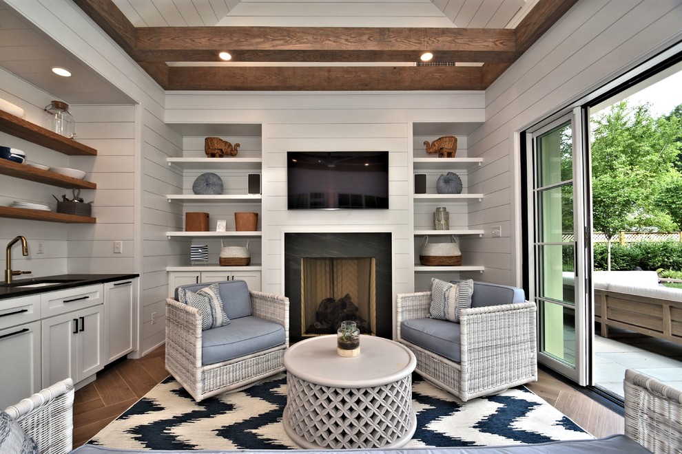Modelo de sala de estar costera con paredes blancas, suelo de madera en tonos medios, todas las chimeneas, televisor colgado en la pared y suelo marrón