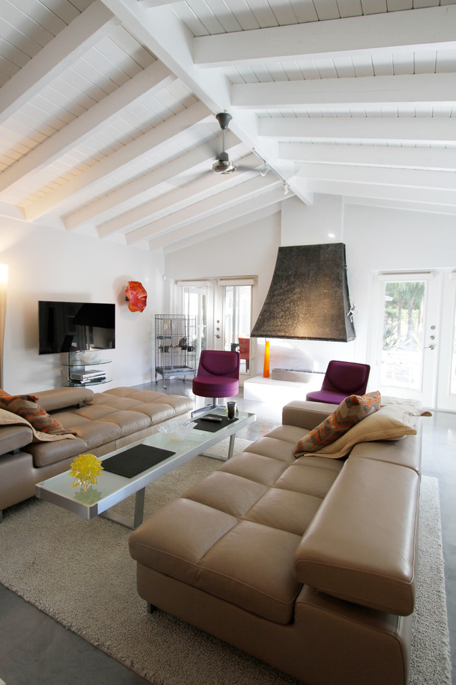 Источник вдохновения для домашнего уюта: большая открытая гостиная комната в стиле ретро с белыми стенами, бетонным полом, двусторонним камином, телевизором на стене и серым полом