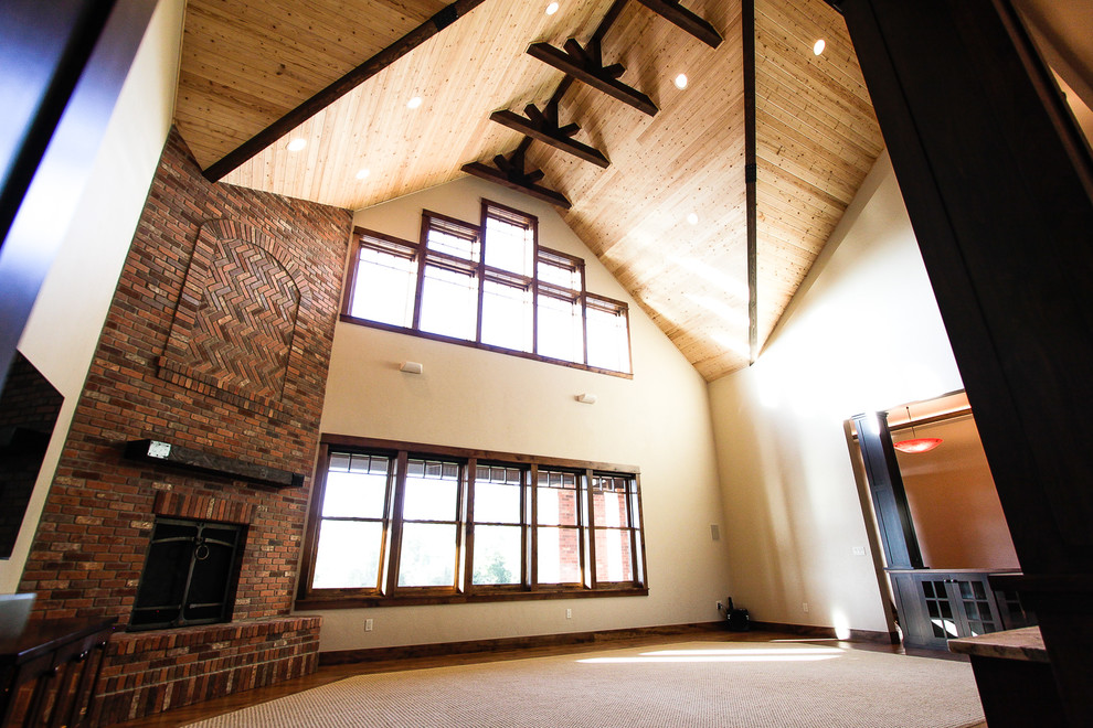 Modelo de sala de estar abierta de estilo americano grande con suelo de madera clara, marco de chimenea de ladrillo y pared multimedia