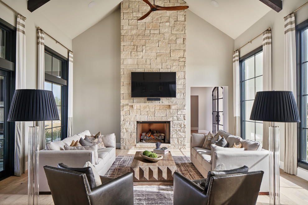 Imagen de sala de estar abierta tradicional renovada con paredes grises, suelo de madera clara, todas las chimeneas, marco de chimenea de piedra y televisor colgado en la pared